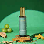 Ayni Ayurveda Hair Renewal Serum bottle on a green background with turmeric and other ingredients.
